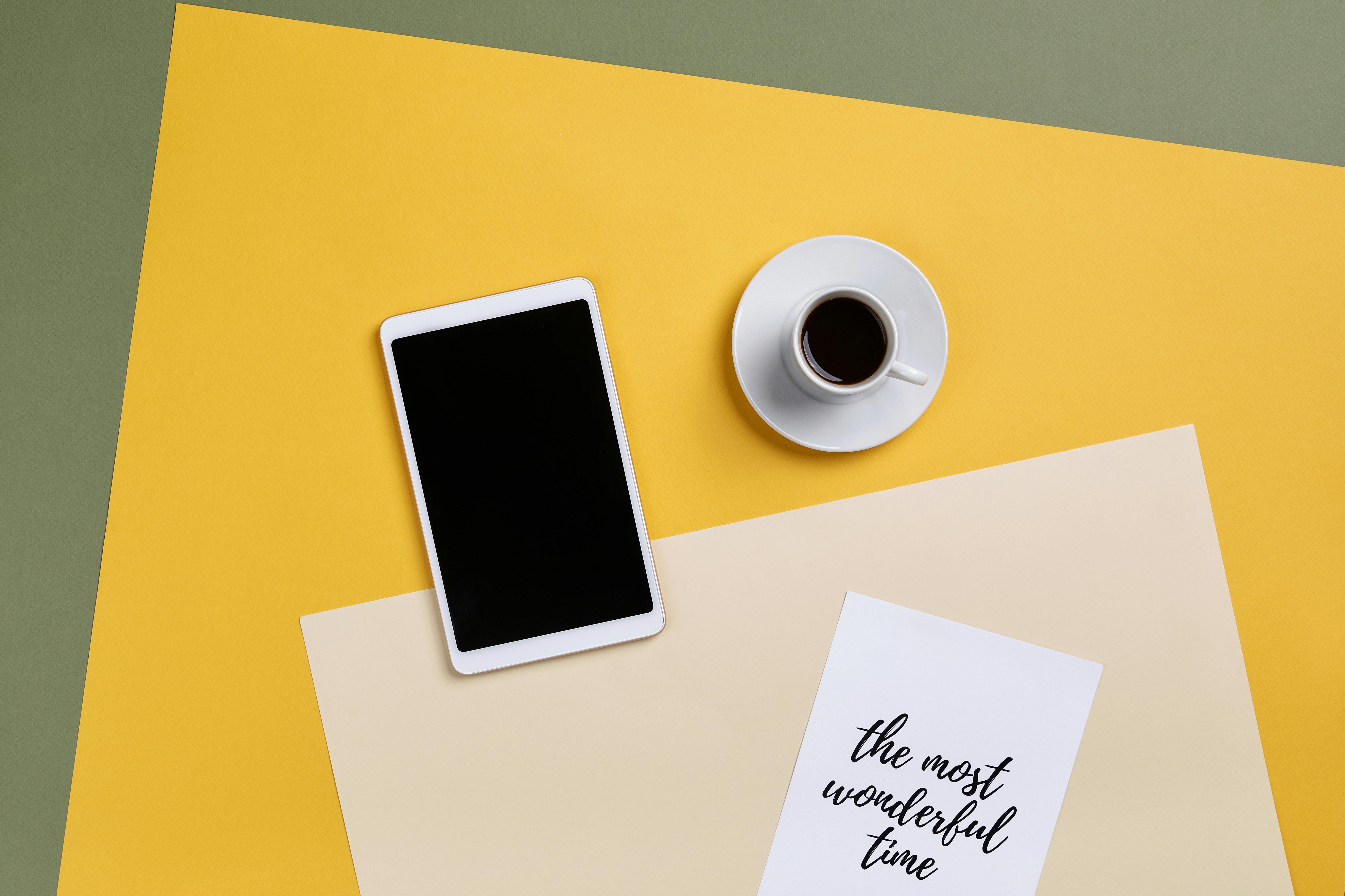 A top view of a minimalist office setup with a tablet, coffee, and paper.