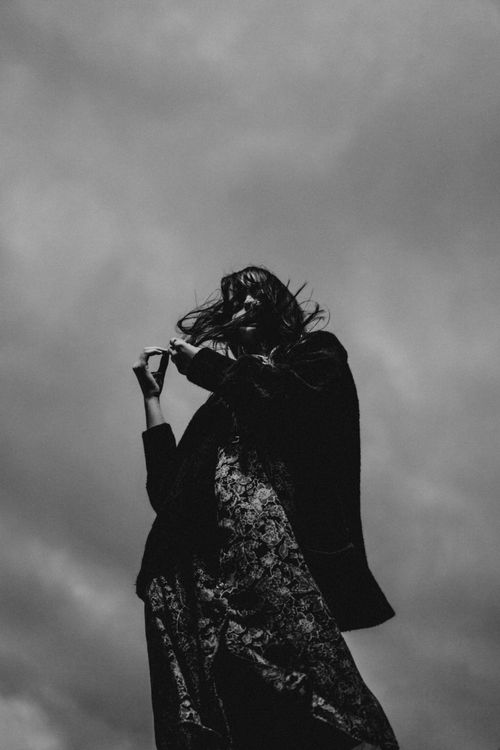 Free A dramatic low-angle black and white portrait of a woman against a cloudy sky. Stock Photo