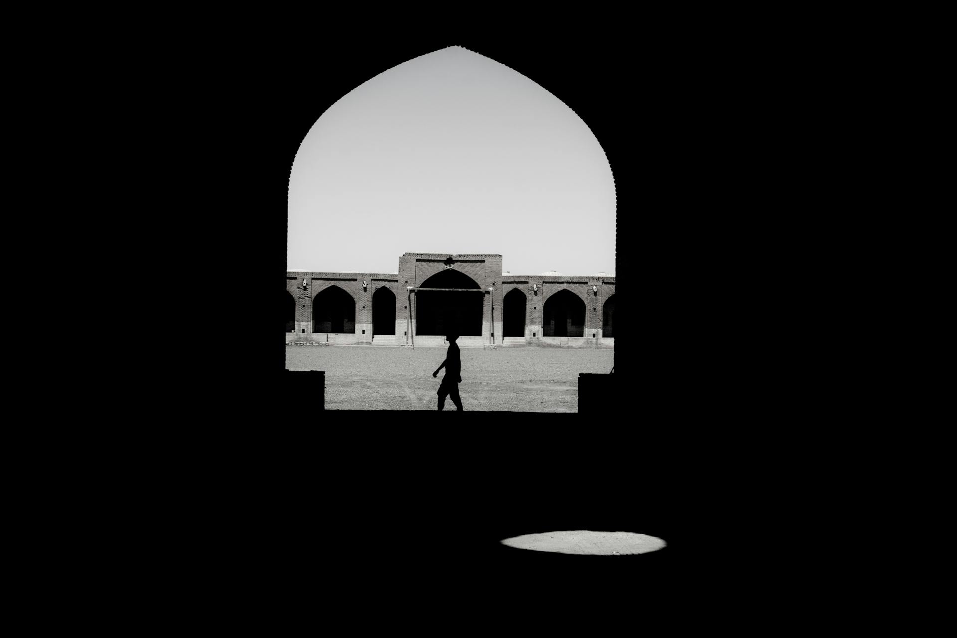 Silhouette in archway frames historic Qom architecture in black and white.