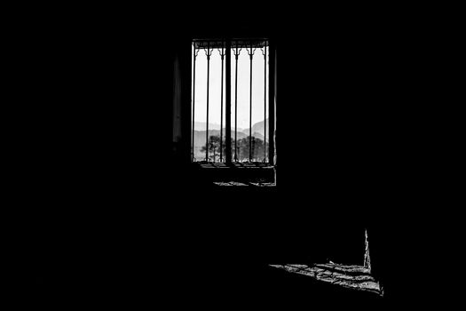 Monochrome shot of a window silhouette overlooking mountains, exuding a dramatic and moody atmosphere.