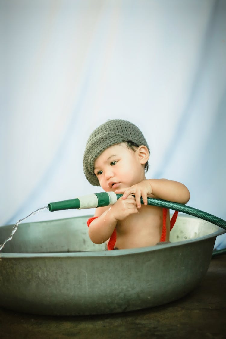 Ethnic Child In Basin Playing With Water Hose