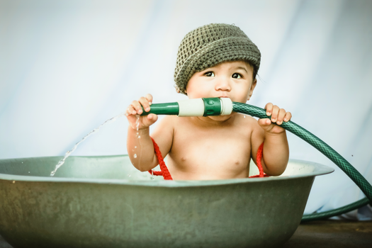 Cute little boy biting garden hose