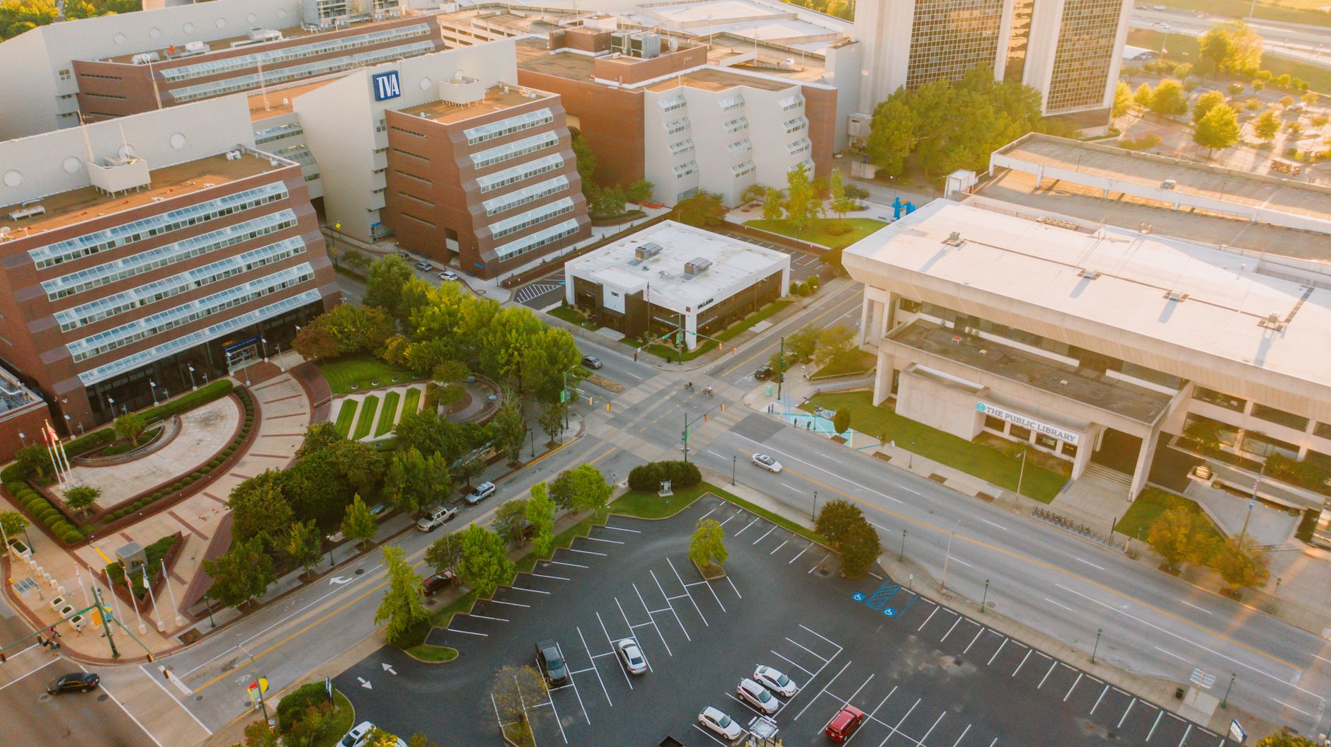Drone view of parking lot with cars located amidst typical modern buildings in city district on sunny day