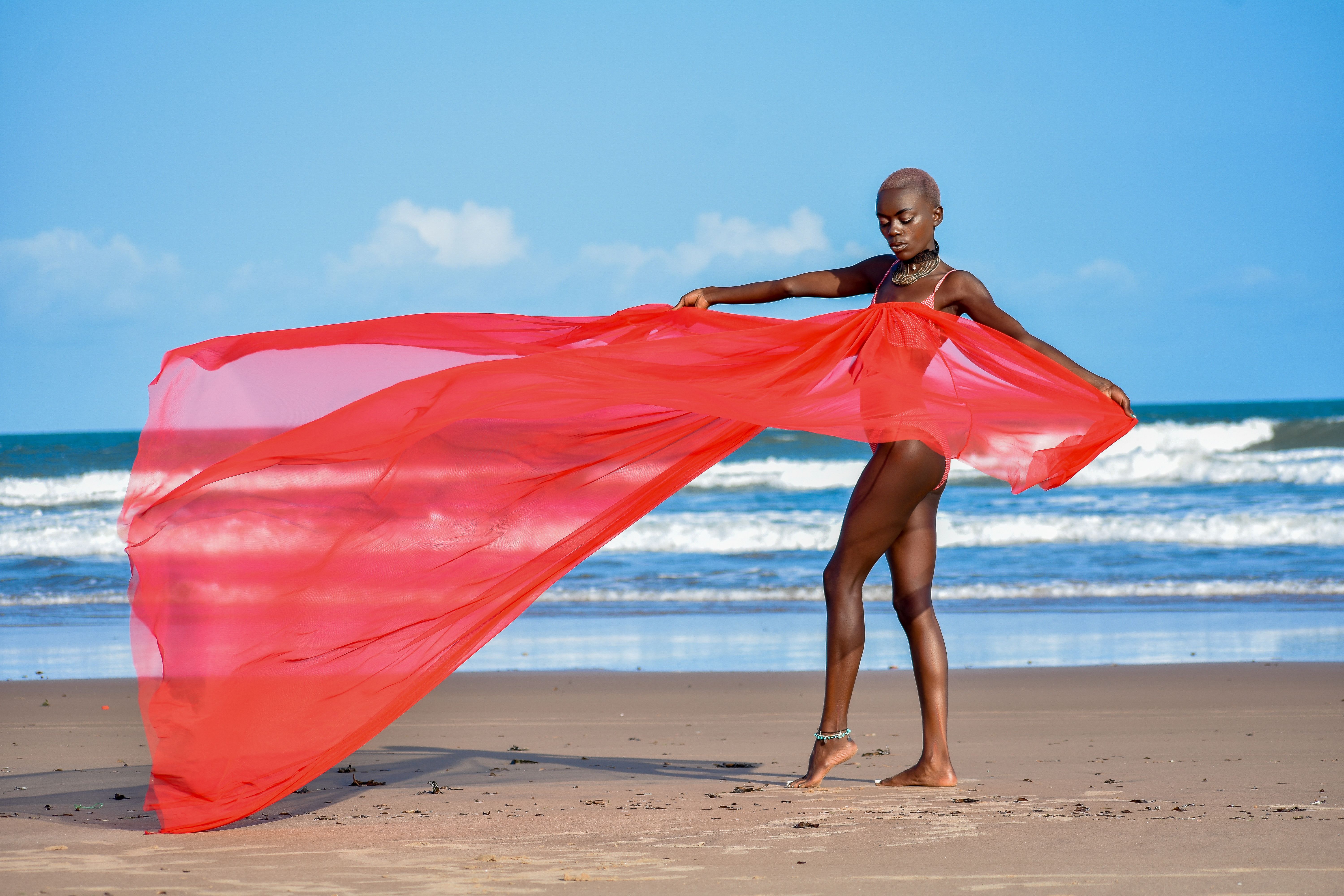 African American woman posing with flowing red scarf on a sunny beach. Vibrant and stylish.