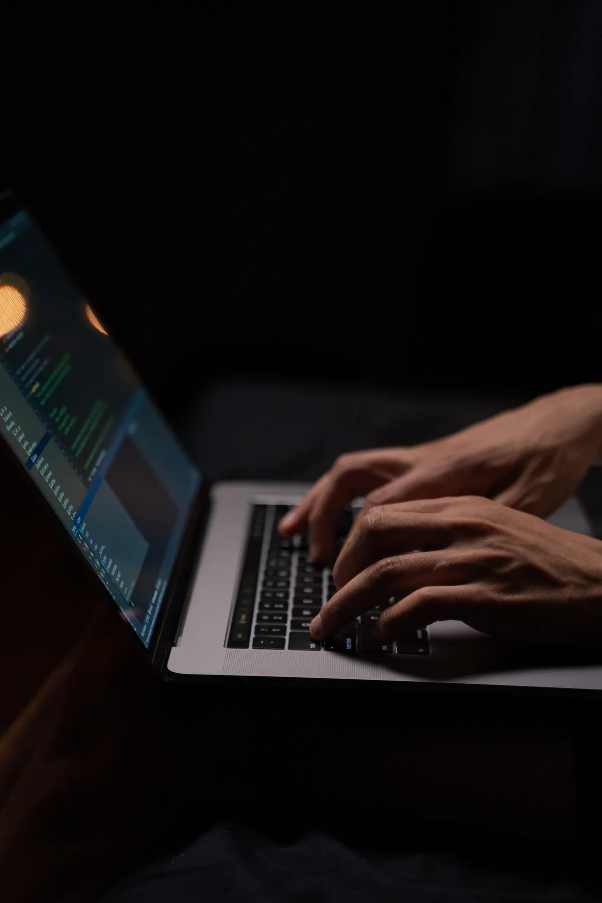 A pair of hands typing code on a laptop keyboard in a darkened room, illustrating a trader prompting ChatGPT for a Pine Script strategy late at night