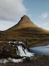 Brown Mountain Near Body of Water Under White Clouds