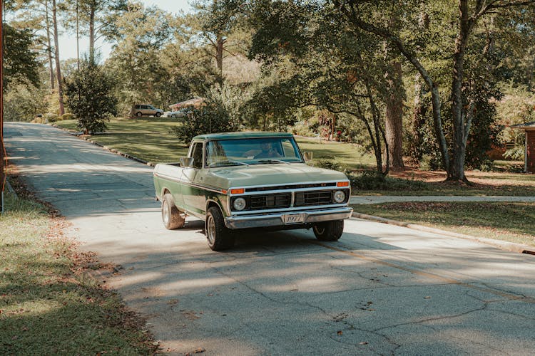 Old Fashioned Pickup Car Driving Along Asphalt Road Amidst Trees