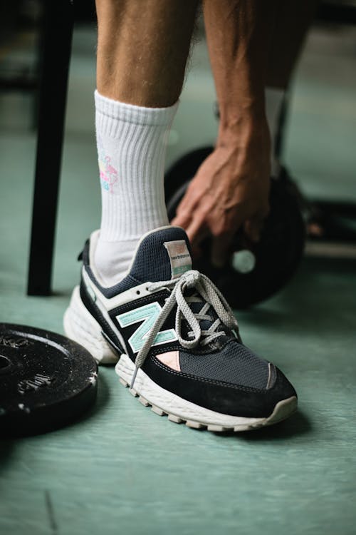 Crop sportsman legs in modern sneakers and socks near black weight plates and dumbbells