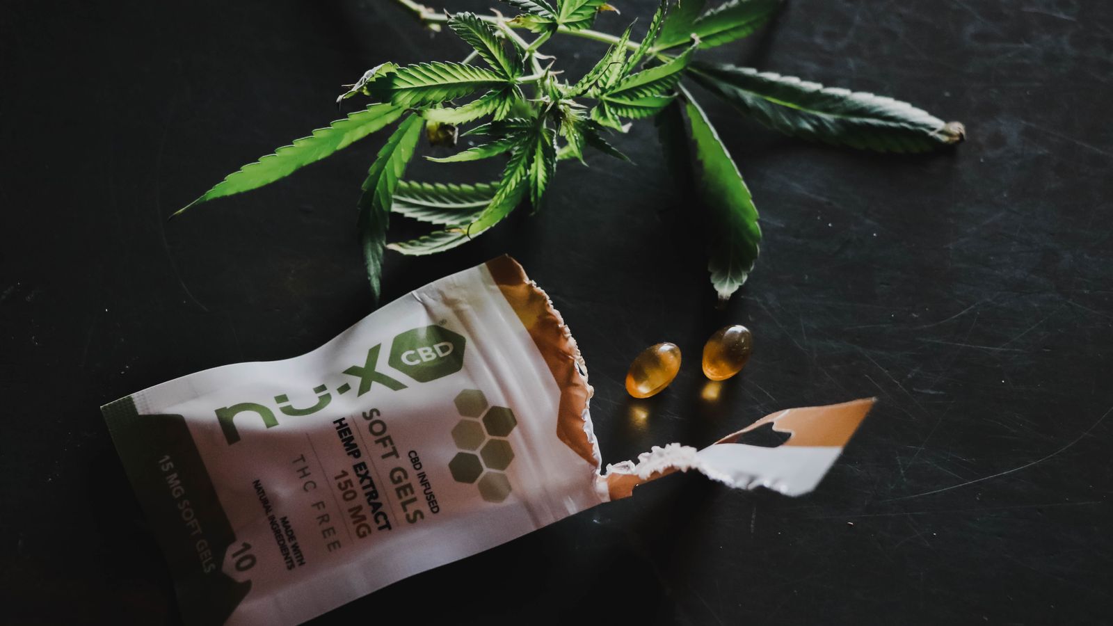 Close-up of CBD softgels with hemp leaves on a dark background.