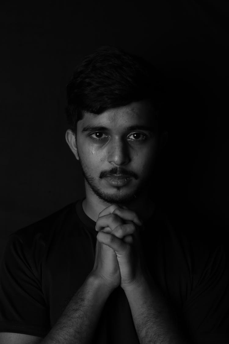 Portrait Of Man With Prayer Hands On Black Background