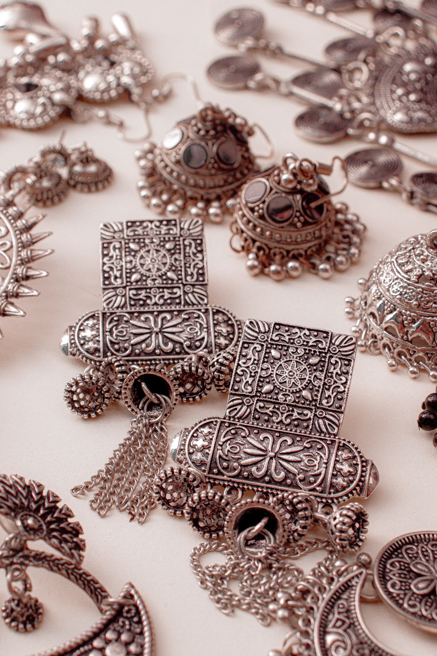 Flat lay of traditional oxidised silver jewellery: jhumka earrings, engraved studs with chain tassels and filigree pieces