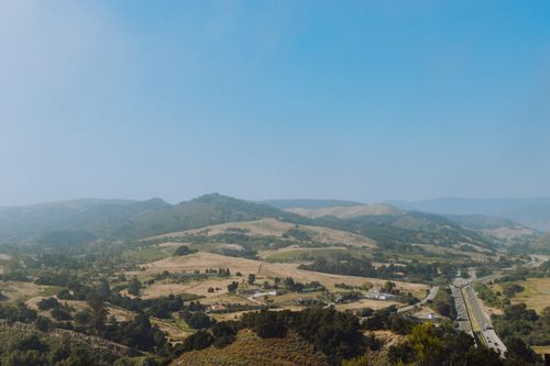 Free Picturesque scenery of hills covered with green trees located near asphalt road under cloudless blue sky Stock Photo