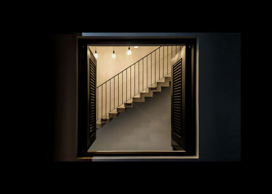 A modern staircase seen through an open window with soft lighting and wooden shutters.