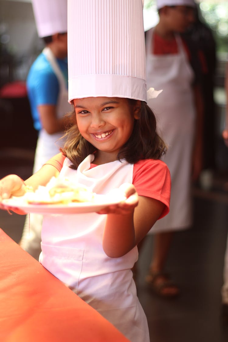 Girl Wearing White Chef Hat Holding A Plate 