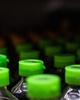 Close-up of plastic bottles with green caps aligned indoors, featuring a blurred background.