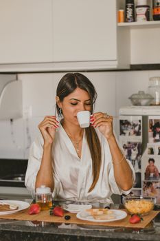 Woman in a white robe savoring a morning coffee in a cozy kitchen setting.