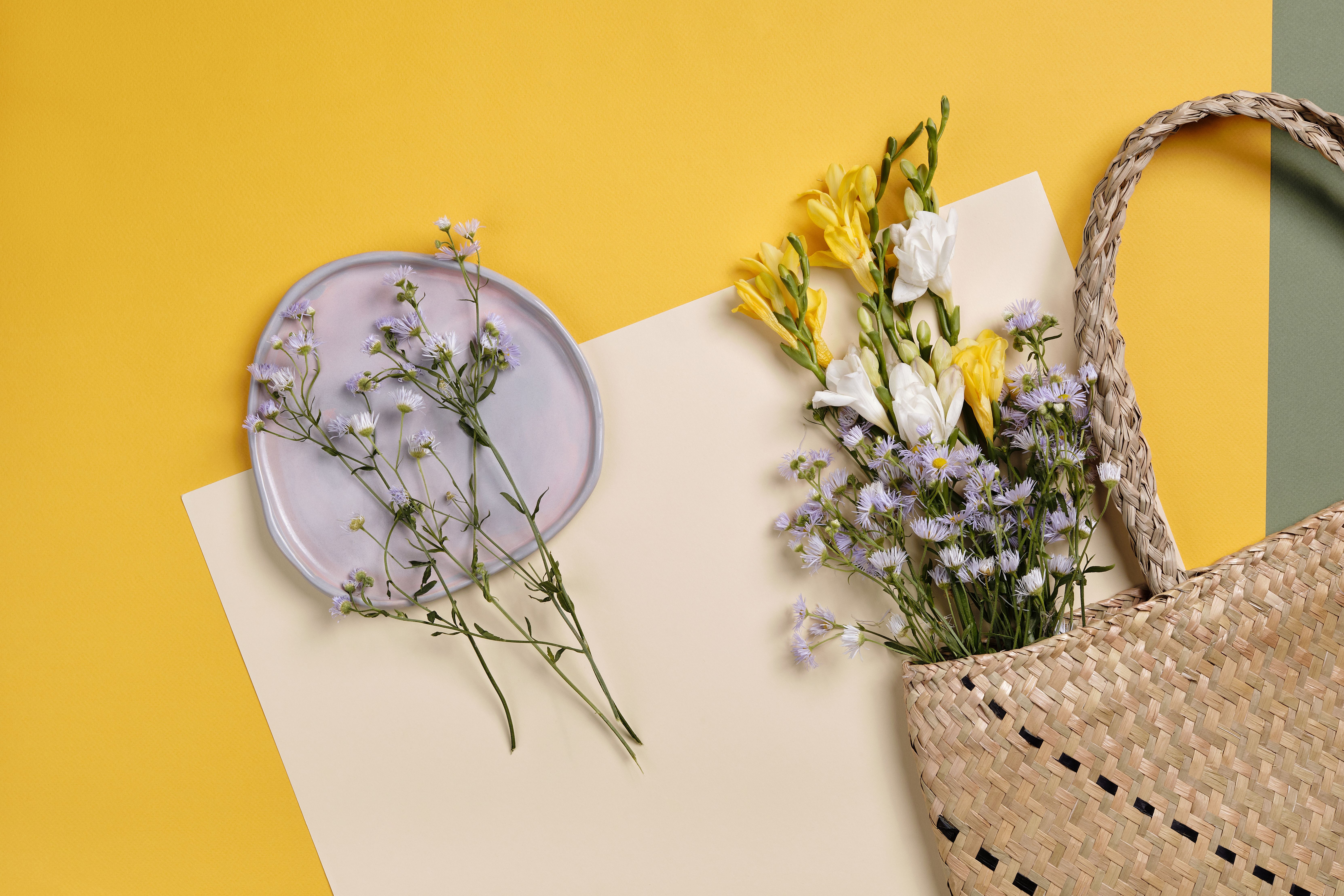 Aesthetic top view of wildflowers and wicker bag on a vibrant yellow background.