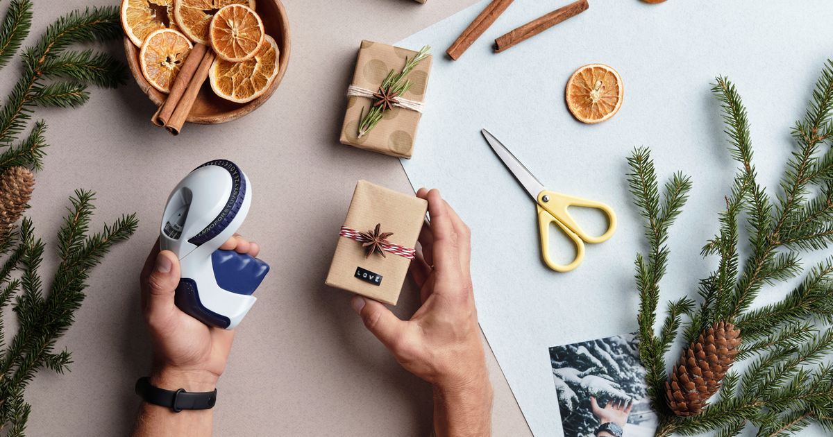 Hands holding a label maker beside a small gift labeled Love, with dried orange slices and pine sprigs