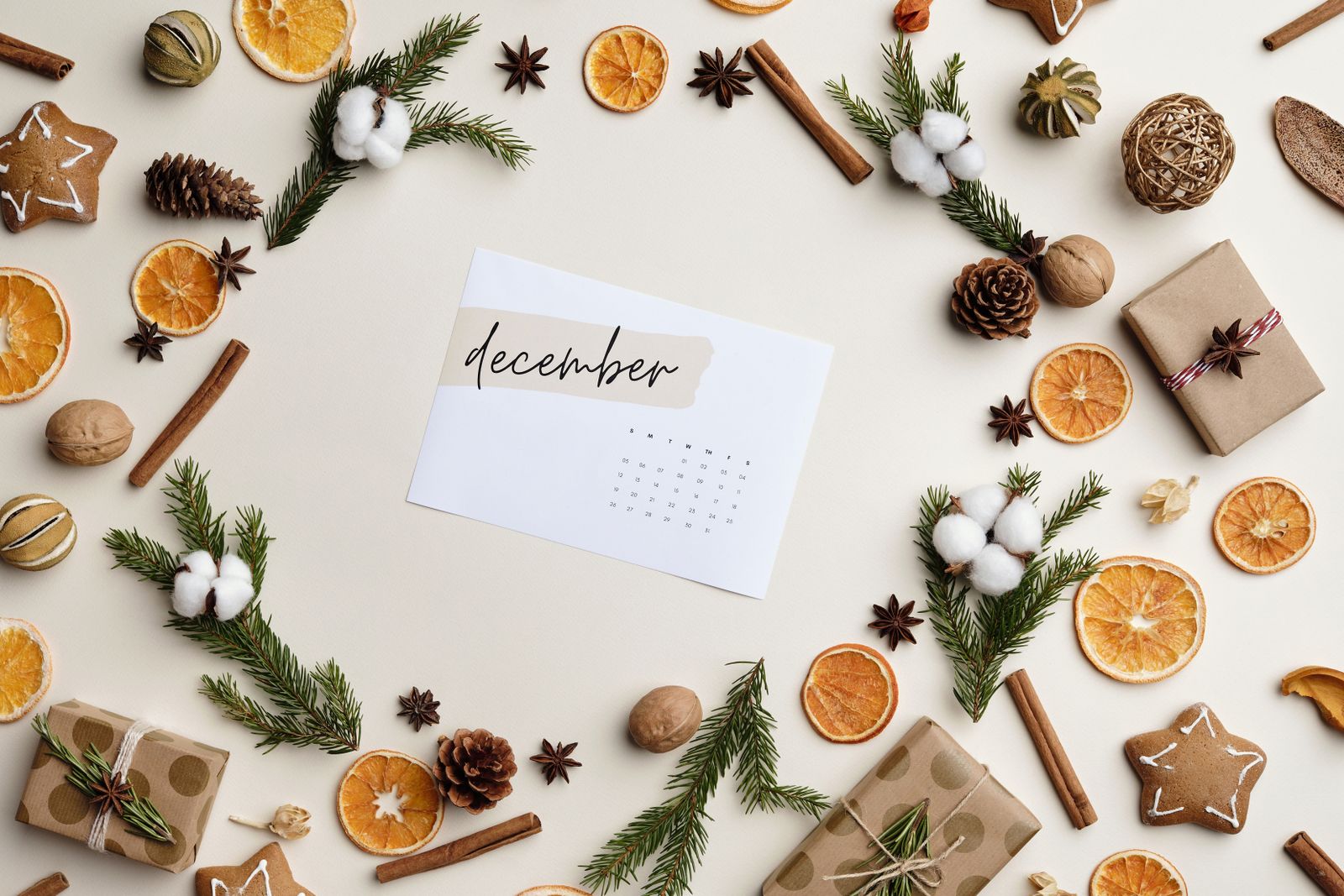 December calendar surrounded by evergreen branches, dried oranges, cinnamon, pinecones, and wrapped Christmas gifts.