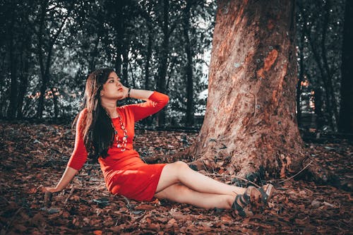 Photograph of a Girl in a Red Dress Sitting Near a Tree