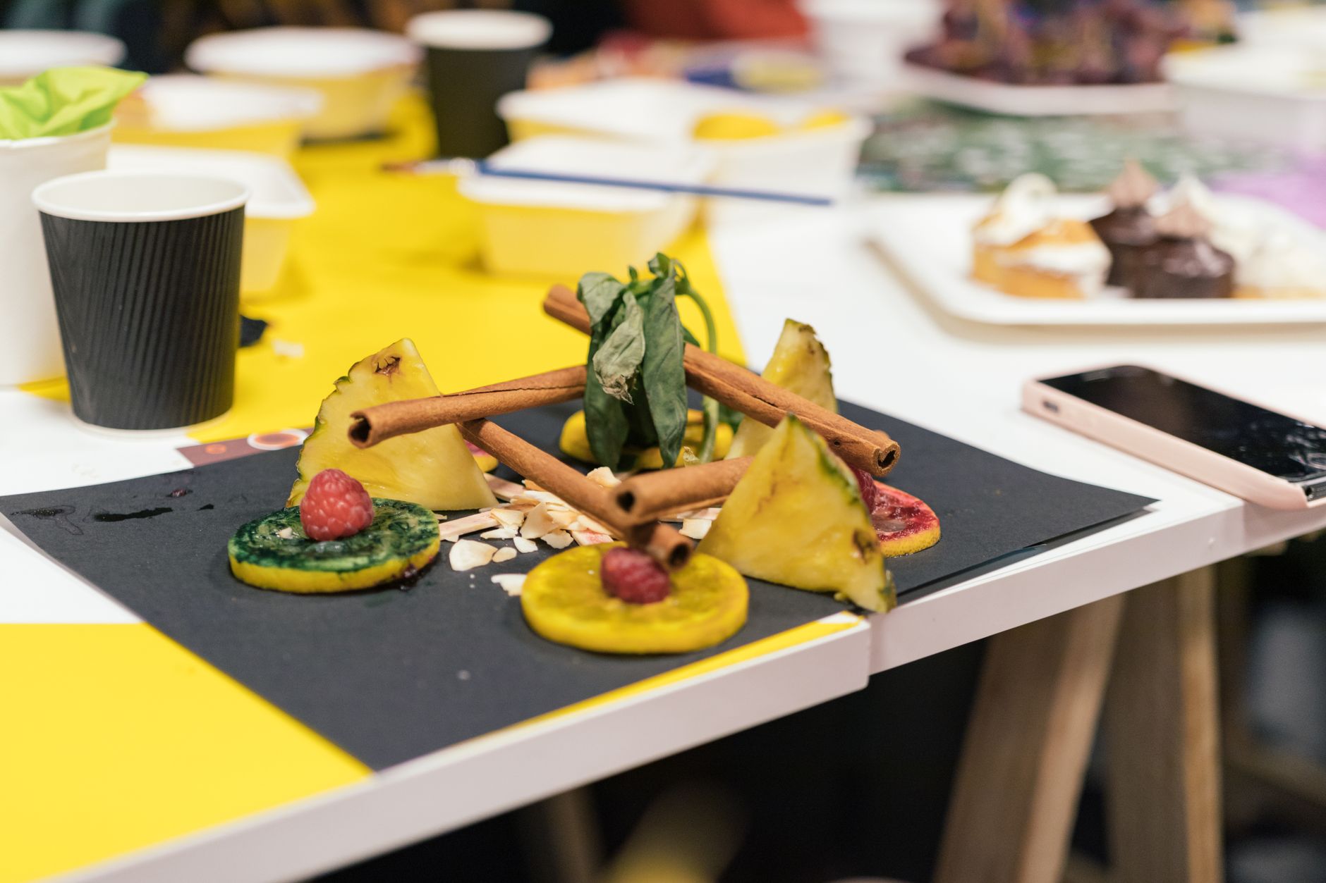 Close-up of artistic food arrangement with fruits and cinnamon sticks on a table.
