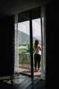 女人站在阳台上，透过玻璃门凝视着宁静的山景