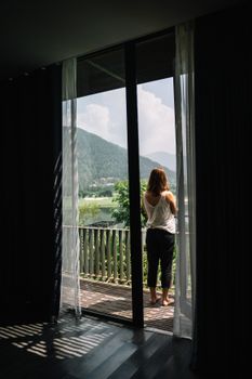 女人站在阳台上，透过玻璃门凝视着宁静的山景