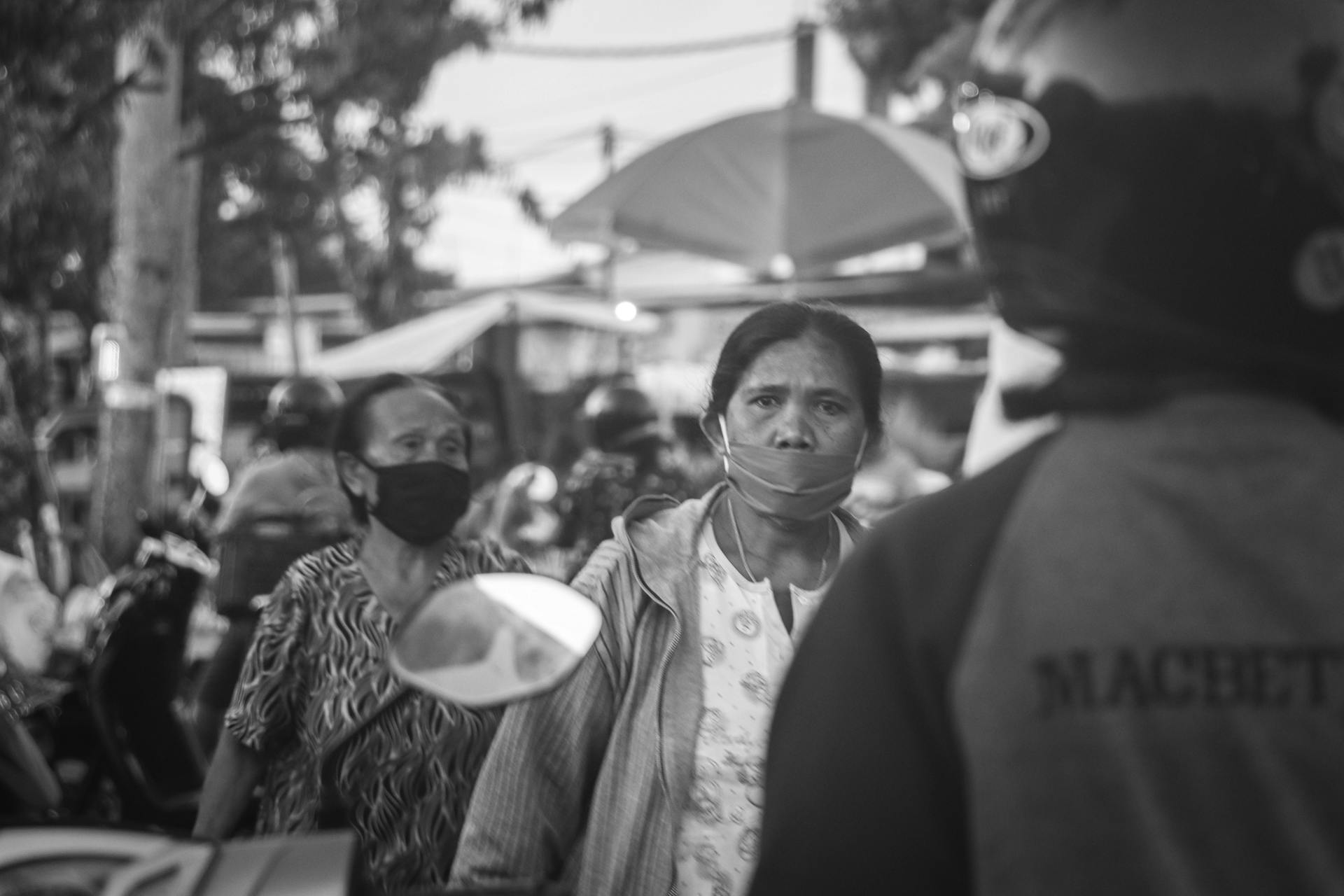 Black and white street scene in Bali showing people with facemasks during the pandemic.