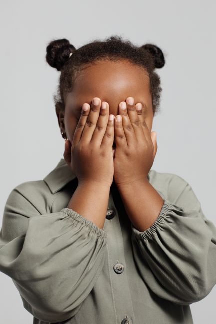 Adorable child with gray sleeves covering face in playful studio pose.