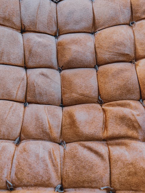 Textured background of aged brown sofa upholstery with thin threads and square shaped ornament