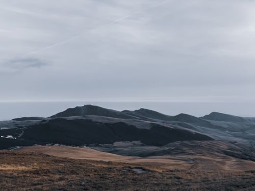 Free Scenery view of ridges near dry barren terrain and ocean under cloudy sky with horizon line in daytime Stock Photo
