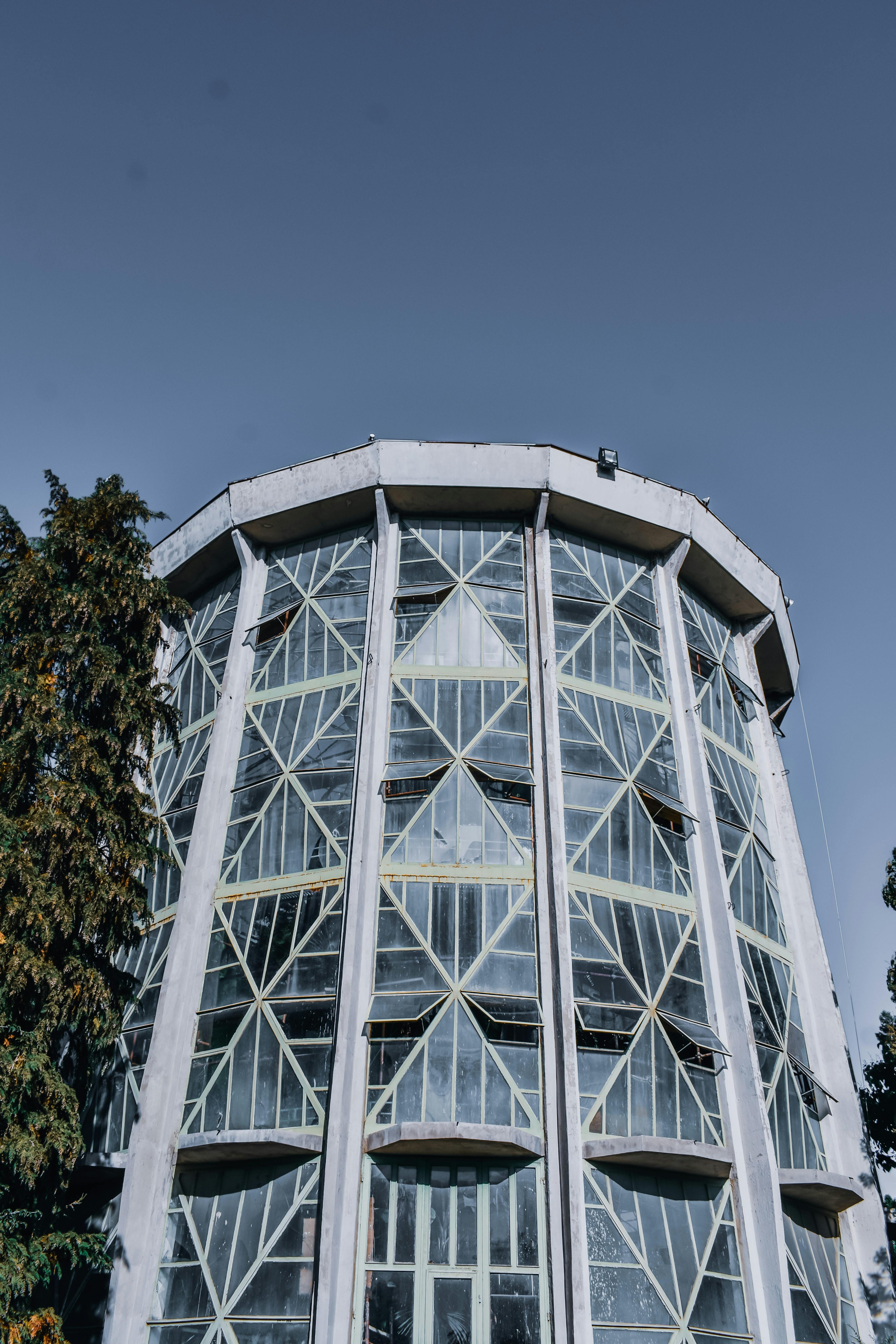 From below of aged tower with decorative walls near trees under cloudless sky in city