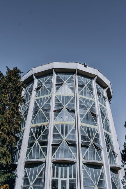 From below of aged tower with decorative walls near trees under cloudless sky in city