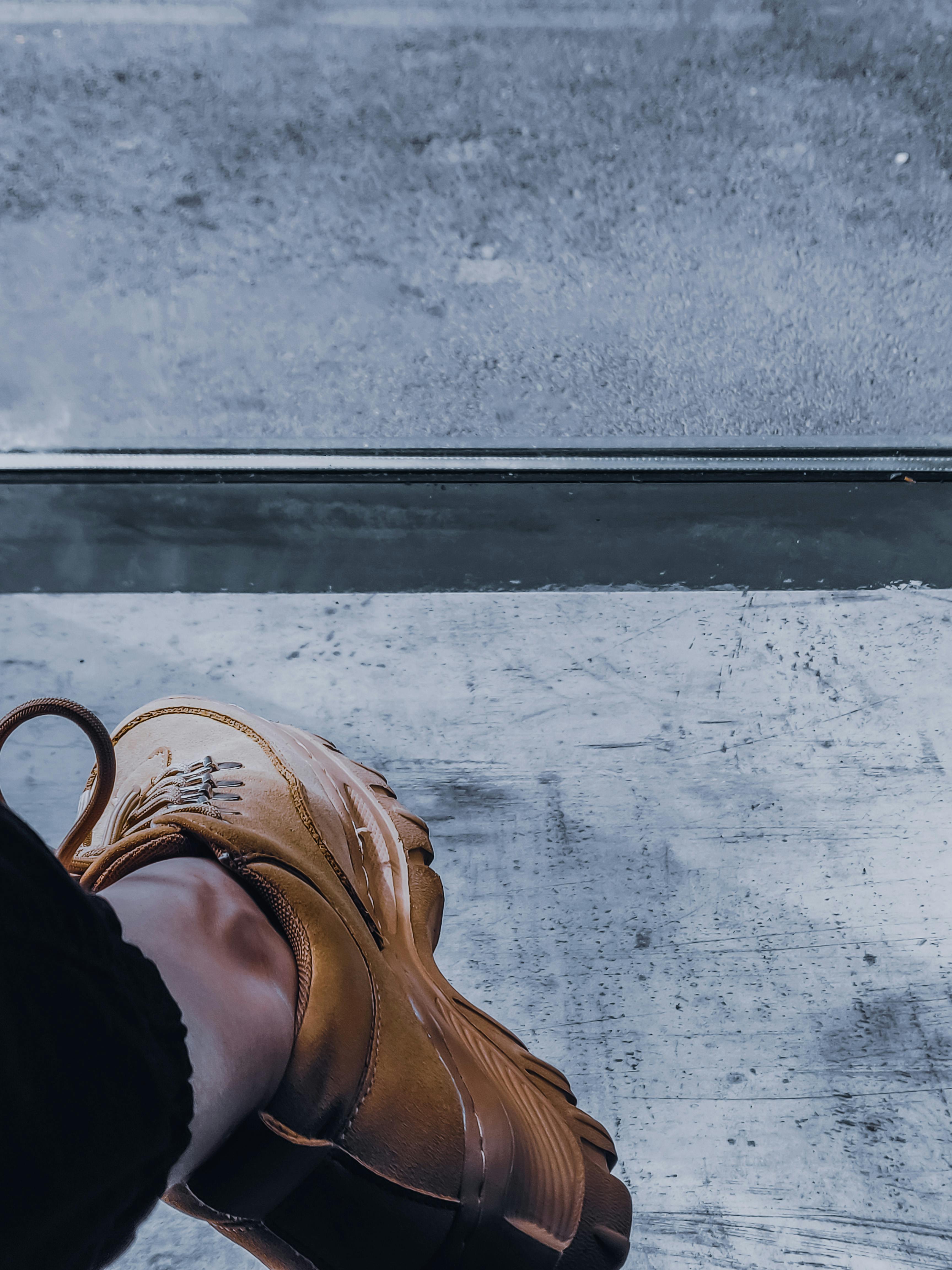 High angle crop unrecognizable person foot in brown suede boot standing on concrete floor