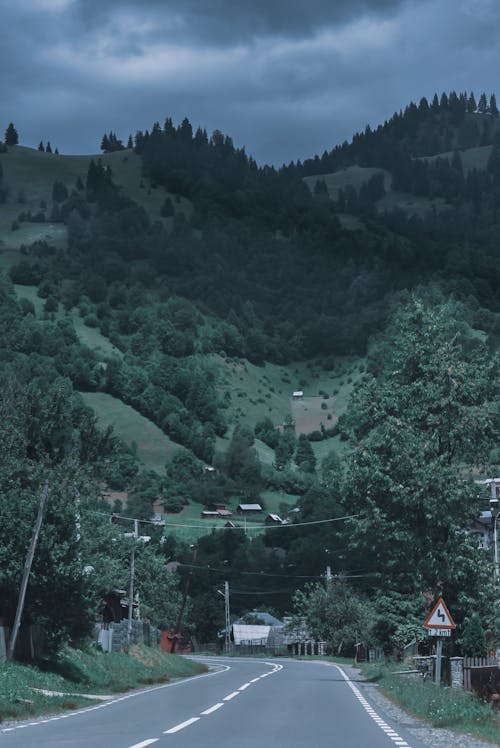 Picturesque scenery of asphalt road running through small countryside located on lush grassy highland under gloomy overcast sky