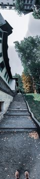 Fish eye faceless person feet standing on narrow asphalt pathway along white countryside buildings on cloudy autumn day
