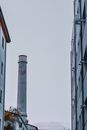 Low angle of tall smokestack pipe near simple buildings in industrial district against foggy sky