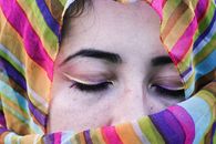 Calm young ethnic female with eyes closed and bright eyeliner on eyelids in vibrant multi colored headscarf in daylight
