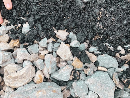 Top view of bunch of small stones and boulders next to dark brown ground in daylight
