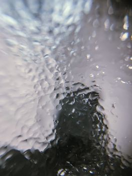 Selective focus of small glistening transparent drops of rain on even surface of glass in daylight