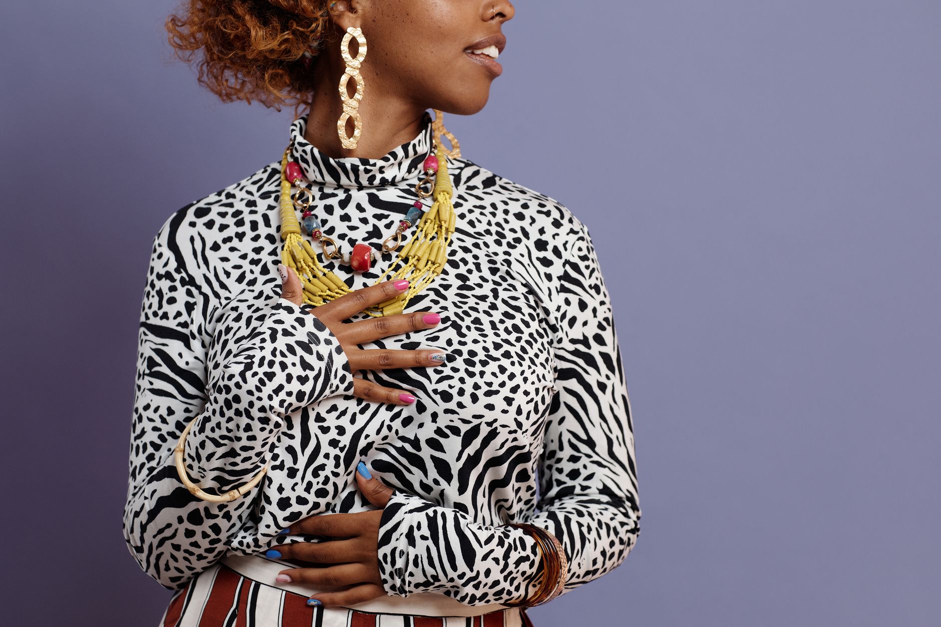 Fashionable woman with jewelry and leopard print outfit posing against a purple background.