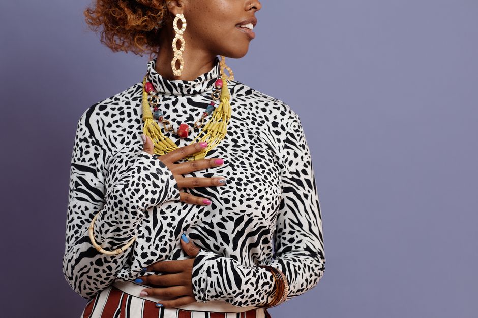 Fashionable woman with jewelry and leopard print outfit posing against a purple background.