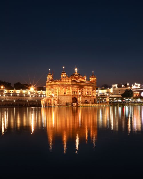 Free Illuminated medieval Sikh gurdwara golden temple located near pond with light reflecting on water at night time in city street in India Stock Photo