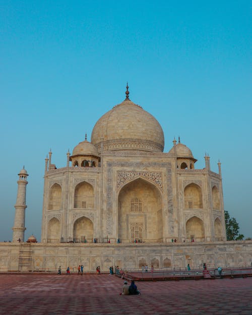 Ancient stone Taj Mahal with dome and fence located on square against blue sky in street in city in India