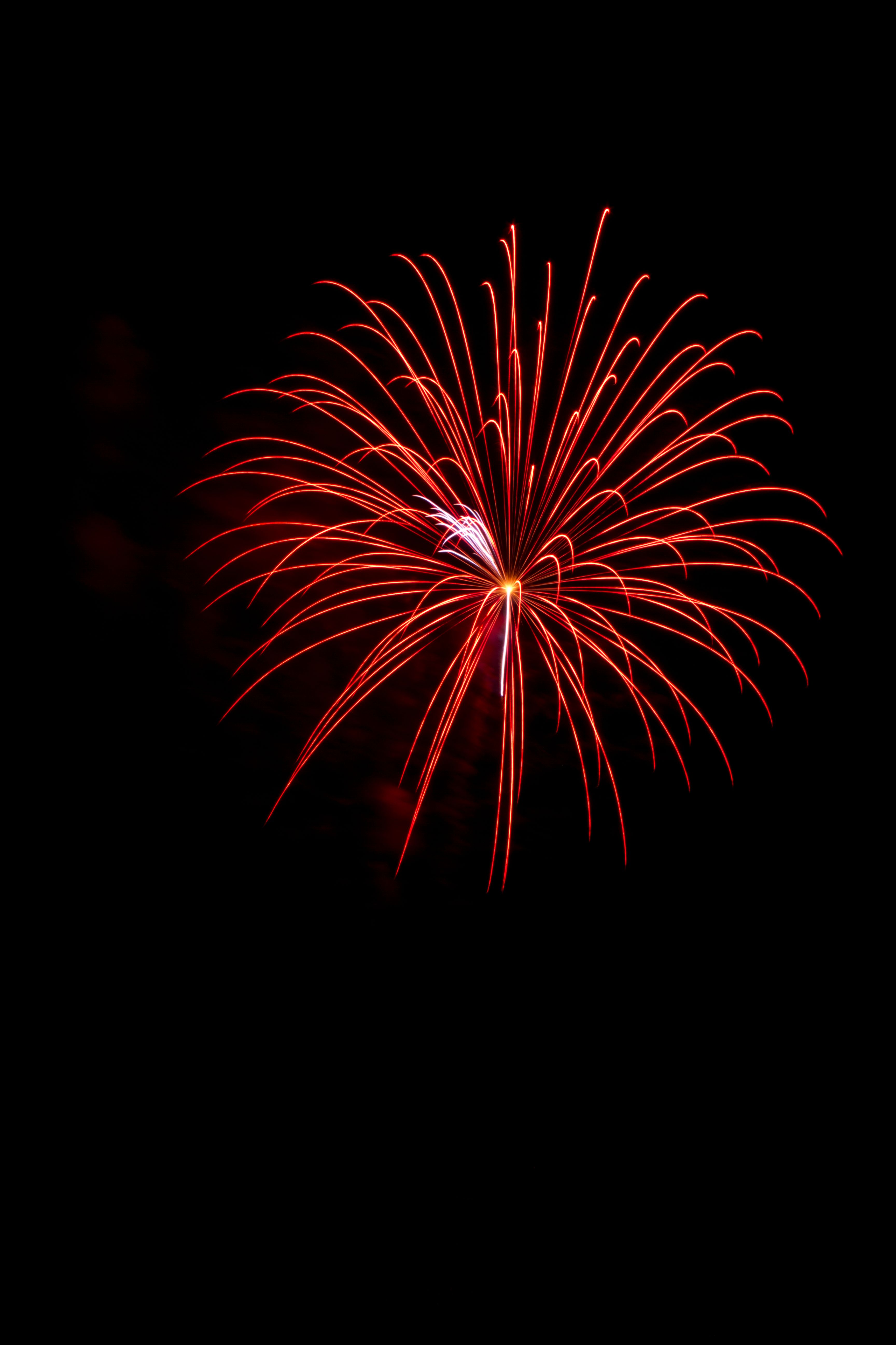 A bright red firework explodes against a dark night sky, perfect for celebrations.