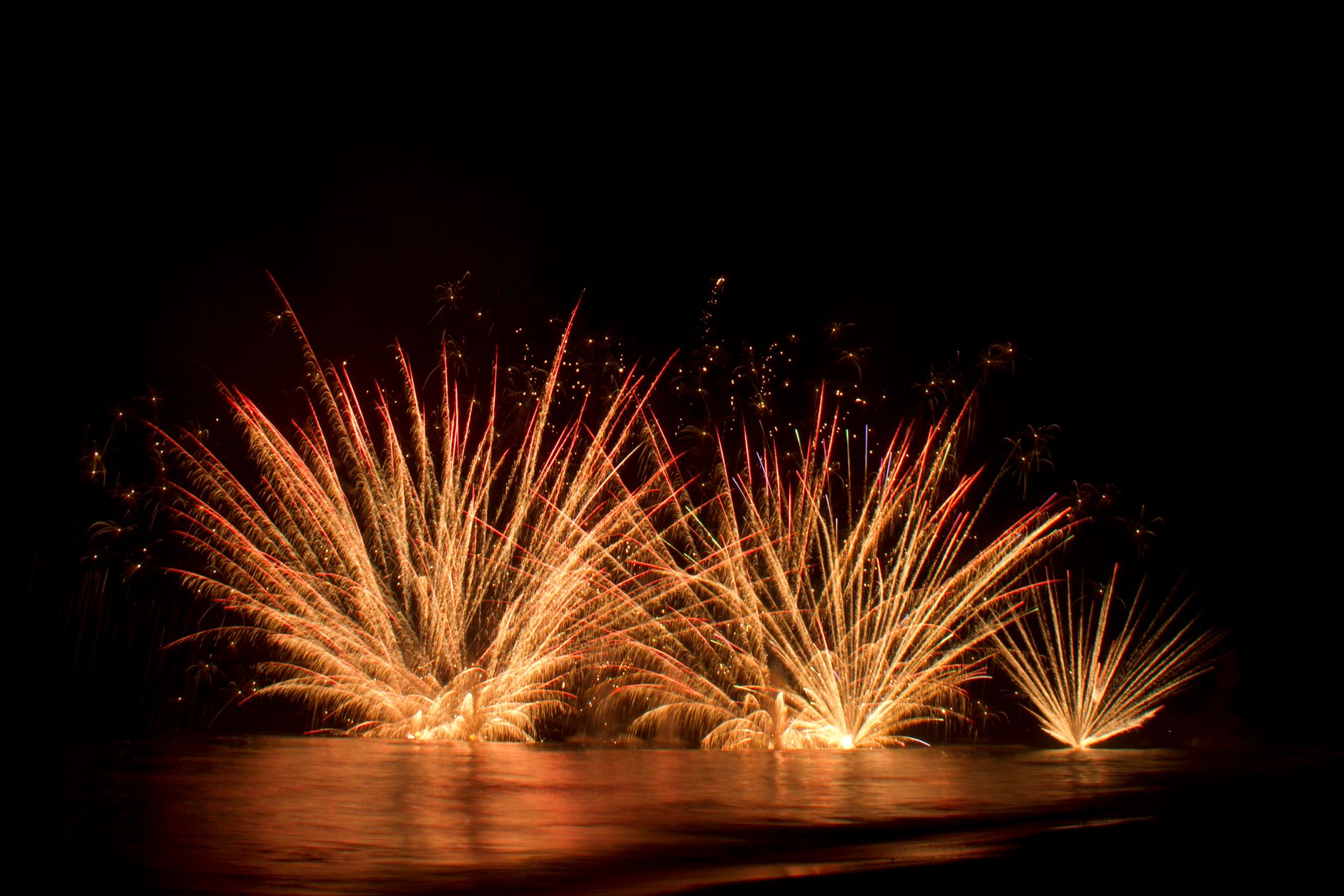 Vibrant fireworks light up the night sky over the ocean, creating a stunning visual spectacle.
