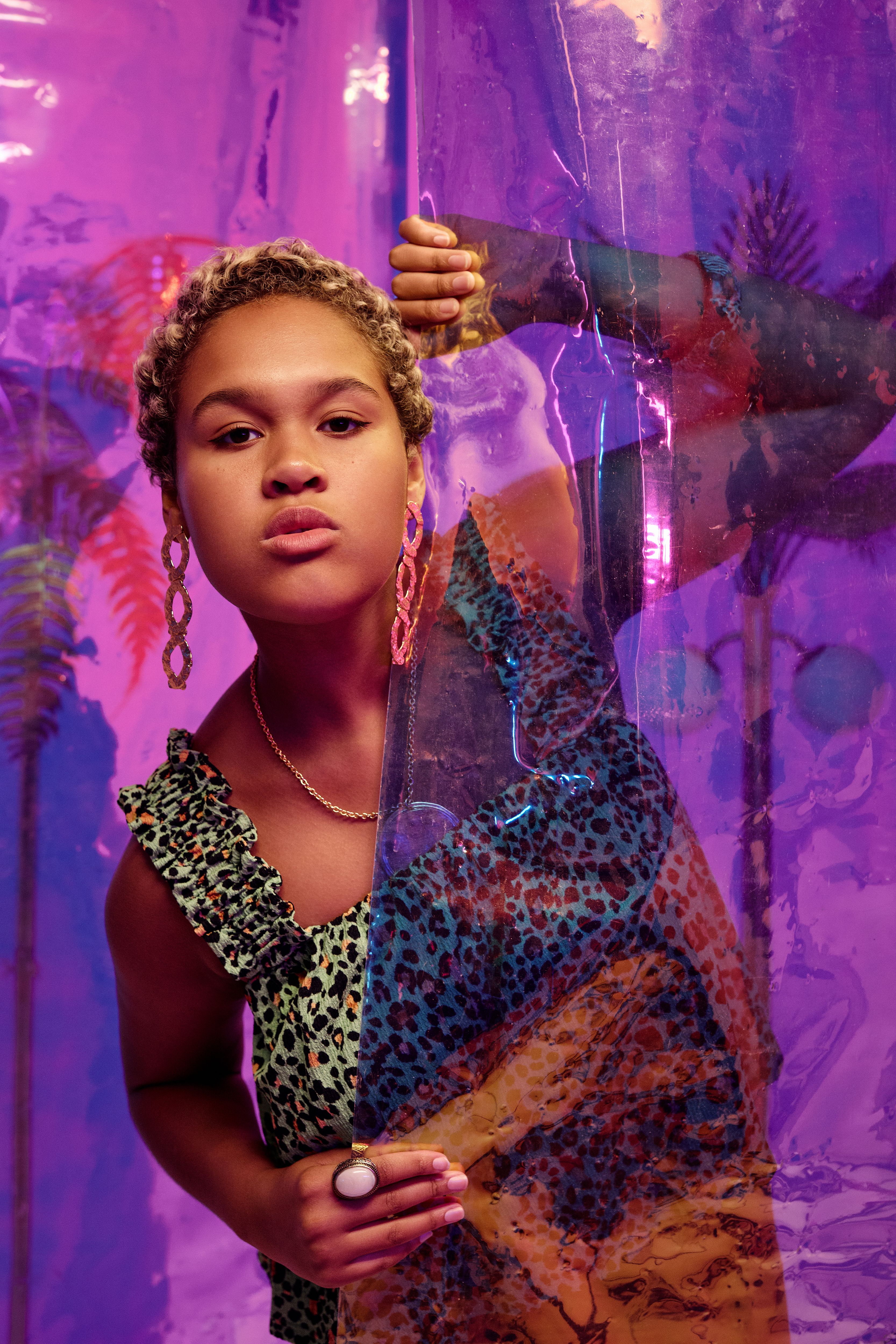 Fashionable woman with afro hair in leopard print dress posing creatively behind a plastic curtain.