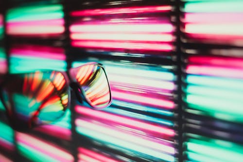 Selective focus of black sunglasses with glossy surface against vivid multicolored blinds in daylight