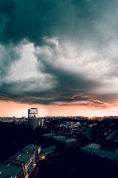 Heavy gray clouds in evening overcast sky over tall multi storey constructions in metropolis at dusk
