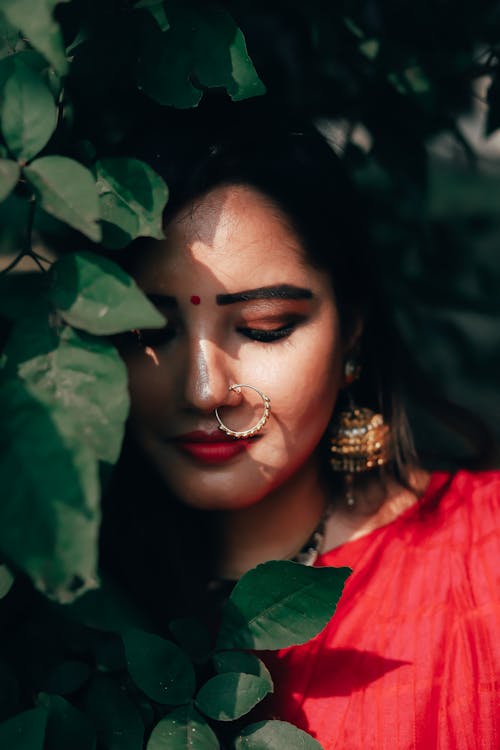 Ethnic female with bindi and massive earrings looking down near lush leaves of green bush